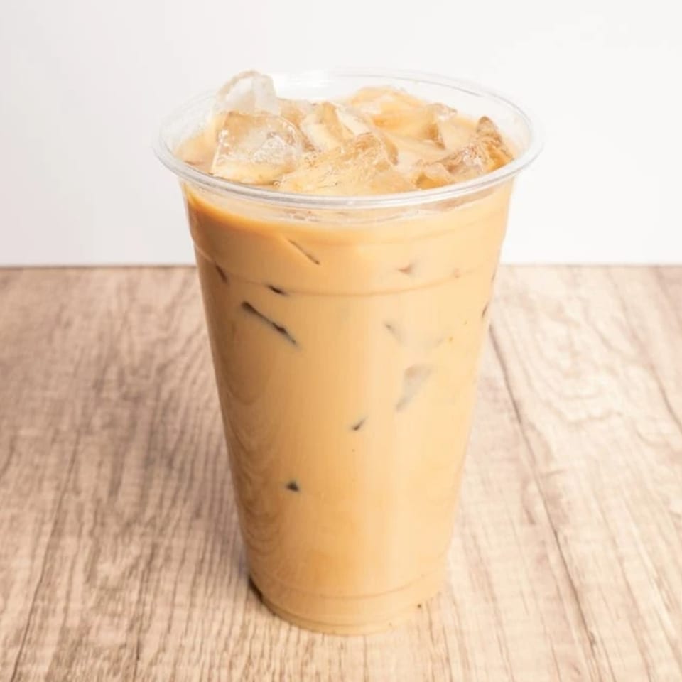 Iced coffee in a clear plastic cup with ice cubes on a light wooden table.