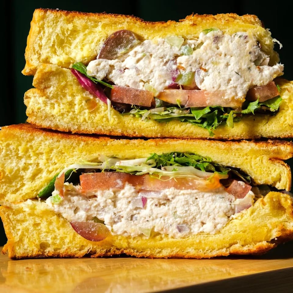 A chicken salad sandwich on toasted brioche bread with lettuce, tomato, and grapes.