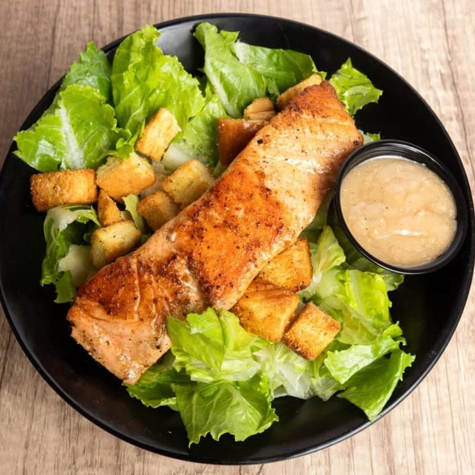 Grilled salmon fillet on a bed of fresh green lettuce with croutons and a side of dressing.