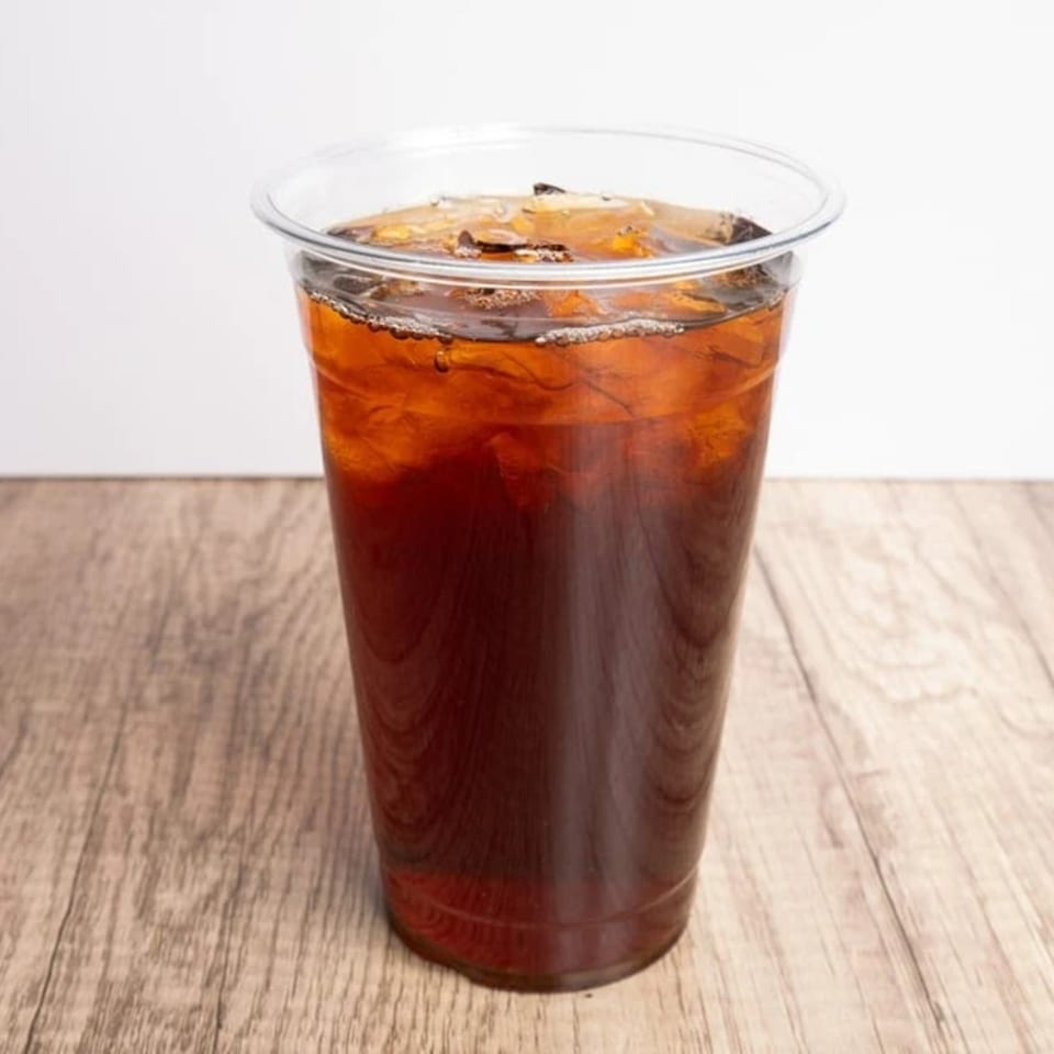 Iced coffee in a clear plastic cup on a light wooden table.