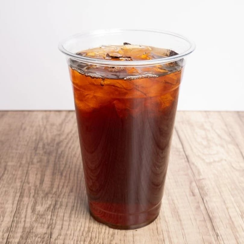 Iced coffee in a clear plastic cup on a light wooden table.
