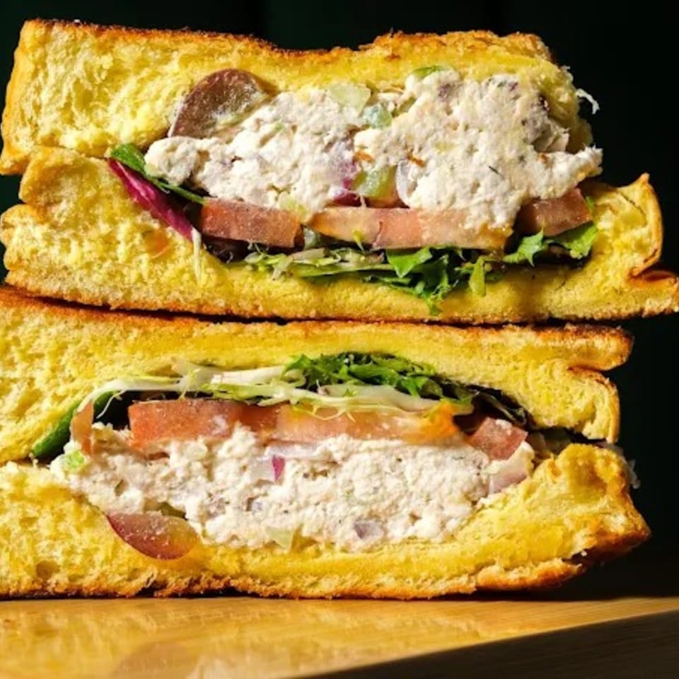 Two halves of a chicken salad sandwich with lettuce, tomato, and grapes on toasted brioche.