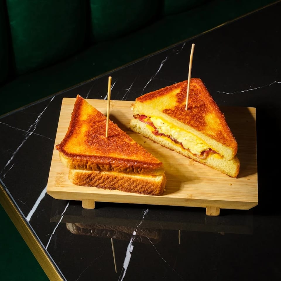 Two halves of a grilled cheese sandwich with bacon and egg, served on a wooden board.