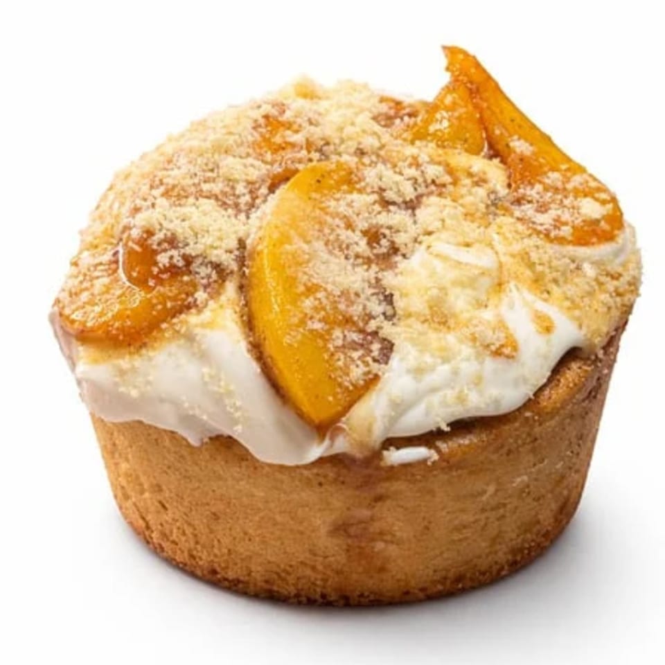 A BOSK coffee muffin topped with whipped cream, sliced peaches, and streusel crumbs.