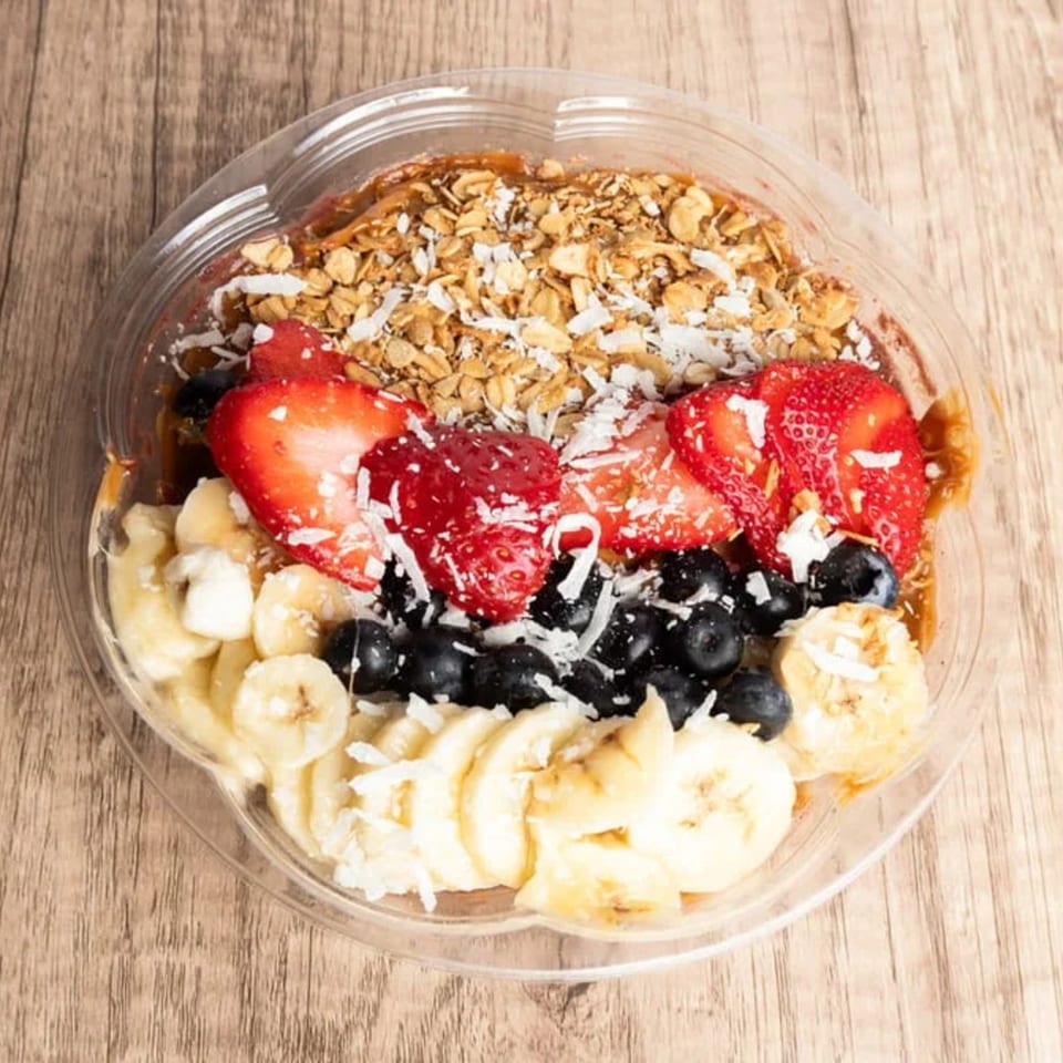 A BOSK acai bowl with granola, strawberries, blueberries, bananas, and shredded coconut.