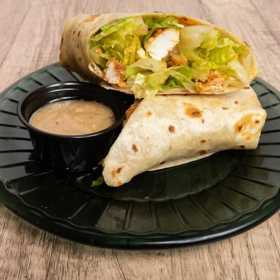 Chicken Caesar wrap with lettuce and a side of dressing on a black plate.